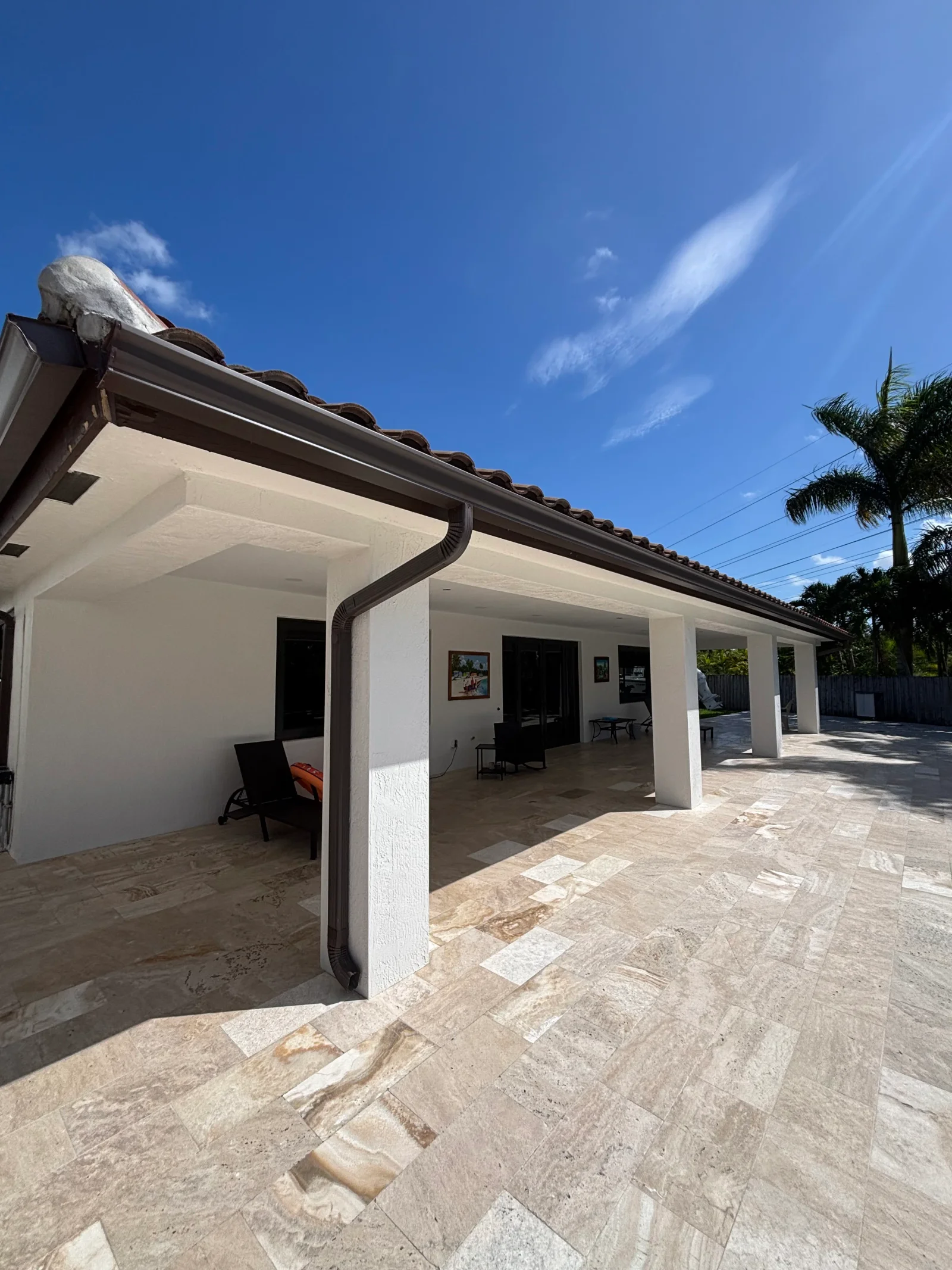 White stucco covered patio with dark trim, travertine tile flooring, and open-air design
