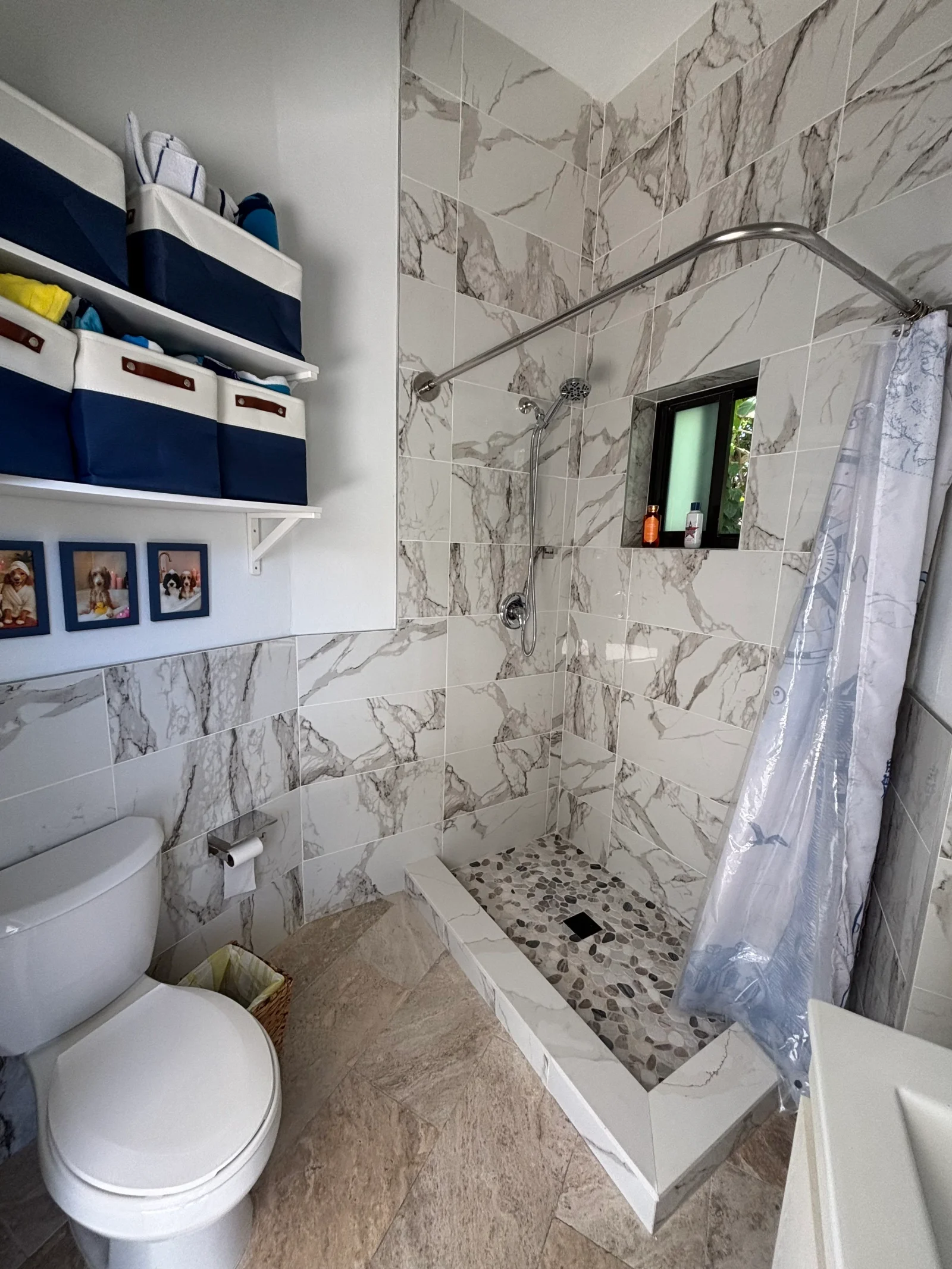 Marble tile bathroom with frameless glass shower, pebble floor, and white shelving