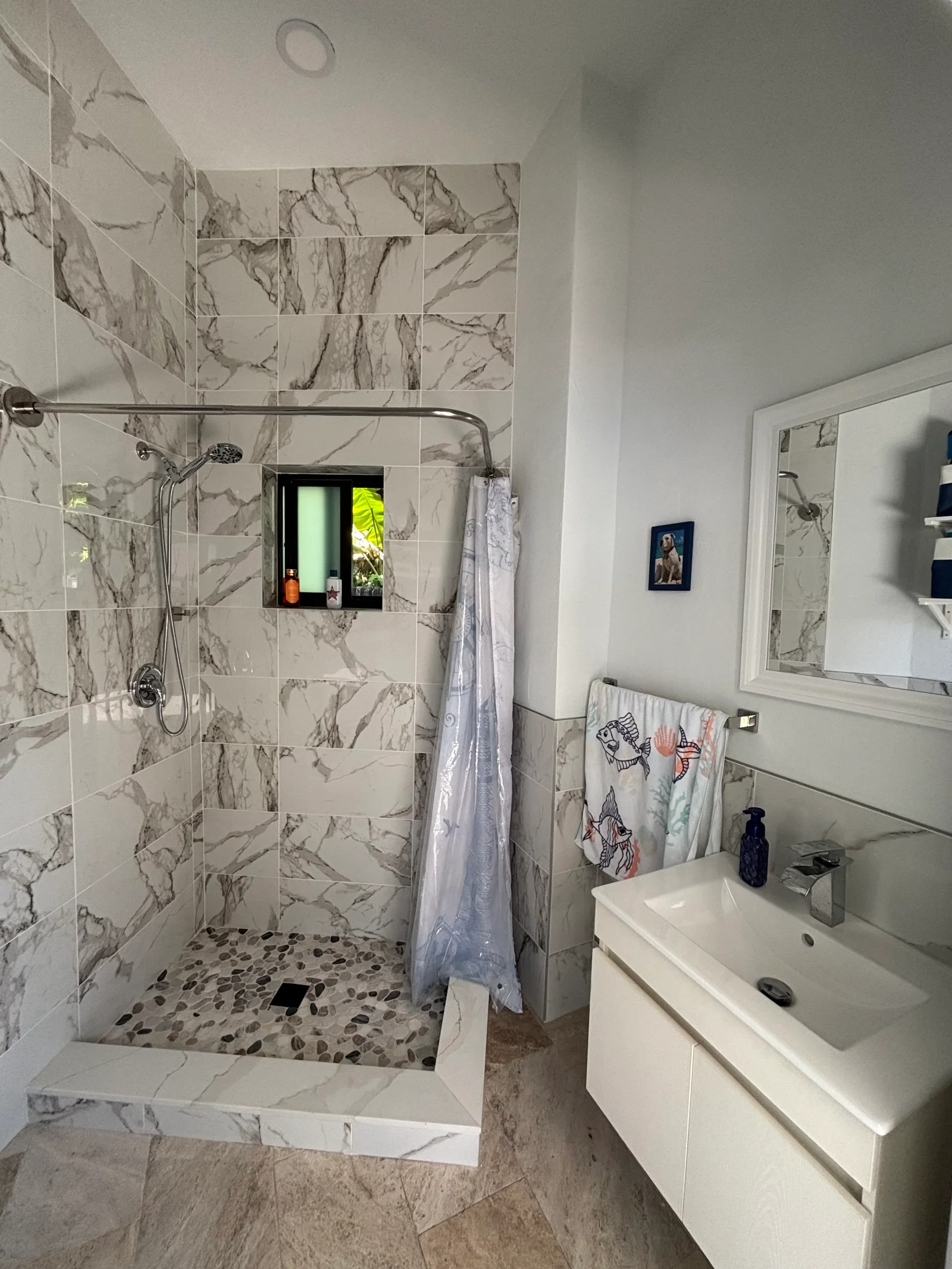 Marble tile shower with pebble floor, glass enclosure, white vanity, and chrome fixtures
