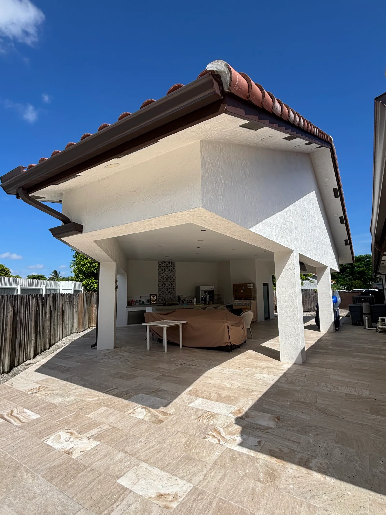 White rendered residential addition with clay tile roof, concrete patio, and open covered living space