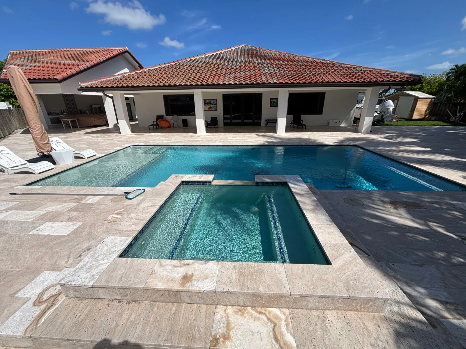 In-ground pool with travertine deck, spa, and modern pool house with clay tile roof